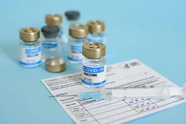 Covid-19 vaccine vial and syringe on CDC vaccination record card on blue background.