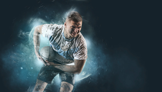 Man rugby player holds ball on smoke background. Sports banner. Horizontal copy space background