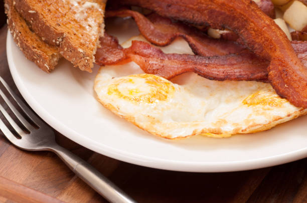 An overhead close up shot of heart shaped eggs inside toast, a couple of bacon strips and fresh squeezed orange juice