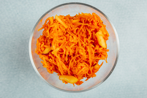 A top view of grated carrot in a glass bowl on a turquoise surface
