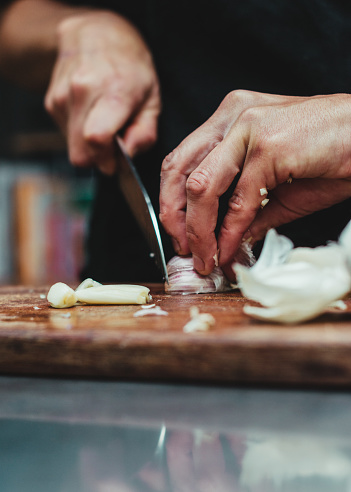 A vertical shot of a chef chopping garlic on a wooden table