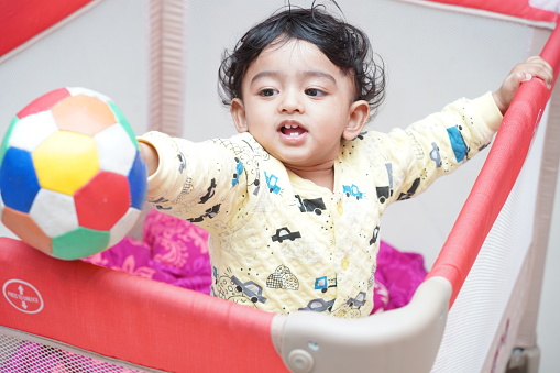An Indian baby boy playing with a colorful ball in his playpen