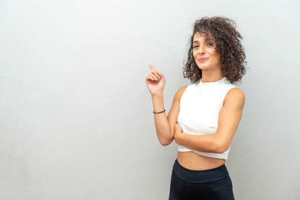 istock Smiling curly haired woman pointing finger at blank wall. 1440990382