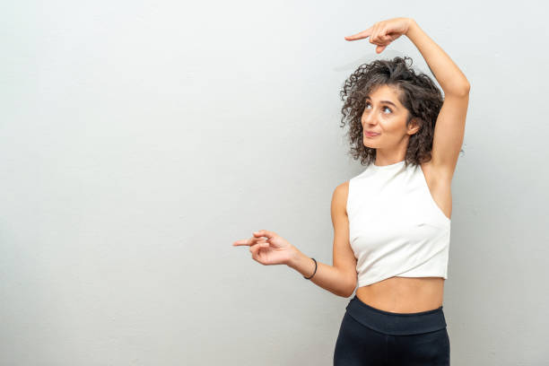 istock Smiling curly haired woman pointing finger at blank wall. 1440990393