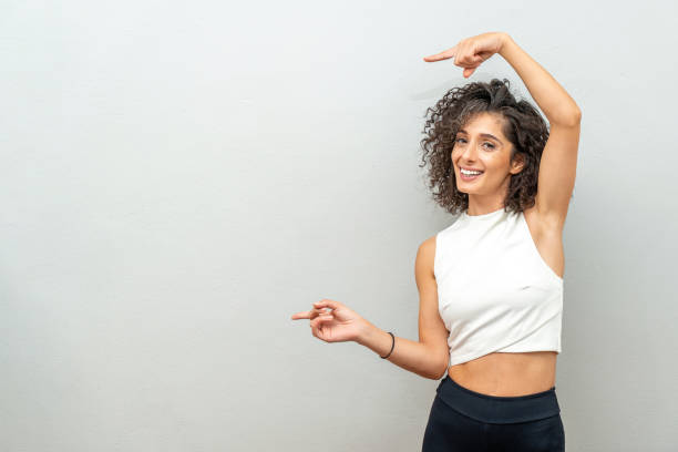 Smiling curly haired woman pointing finger at blank wall.