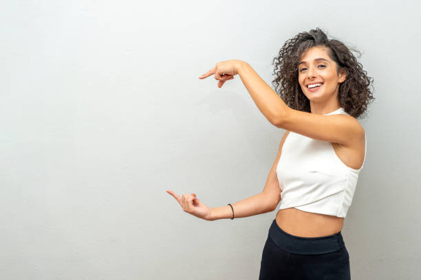 istock Smiling curly haired woman pointing finger at blank wall. 1440990451