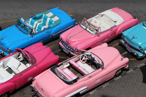 old cuban collectible cars in pink and blue colors parked in old havana
