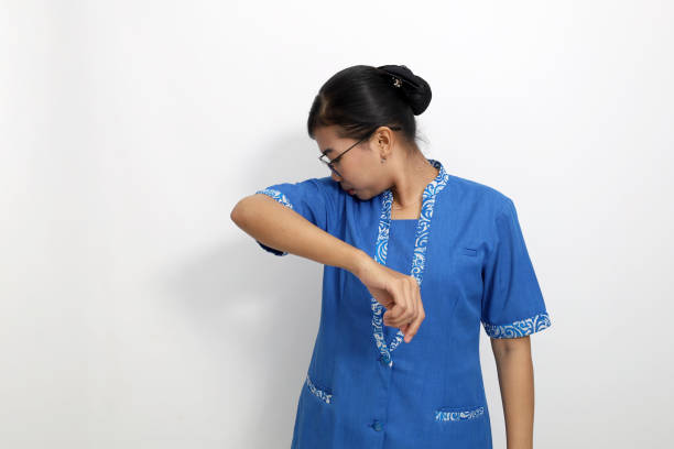 Young asian employee standing while smelling her armpit. Isolated on white background with copyspace
