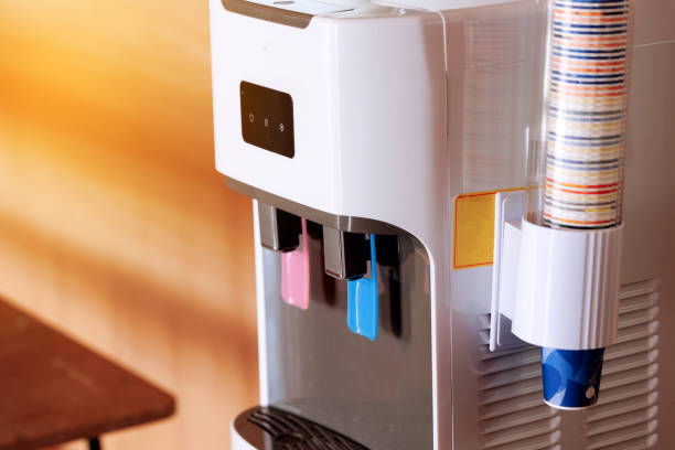 Detail of the two plastic taps for hot and cold water, colour coded, on a electric purified water dispenser. Modern water cooler with paper cups in office. Healthcare concept. Business concept. detalle de los dos grifos de plástico para agua fría y caliente, codificados por colores, en un dispensador eléctrico de agua purificada. moderno enfriador de agua con vasos de papel en la oficina. concepto asistencial. concepto de negocio