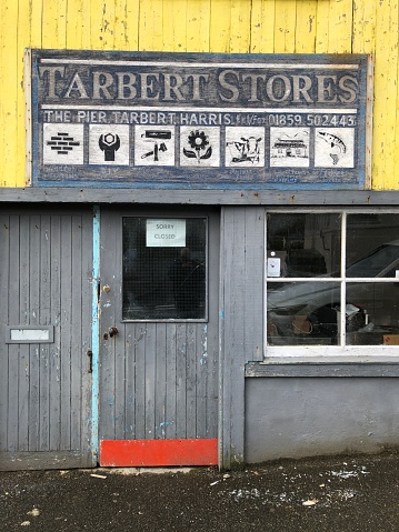 Tarbert, Isle of Harris, Outer Hebrides, Scotland, United Kingdom - April 16, 2022: An old hardware shop in the village of Tarbert with a wooden door, closed for business.