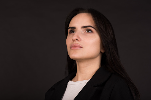 Portrait of a young and serious Armenian brunette girl in a black jacket isolated on a black studio background.