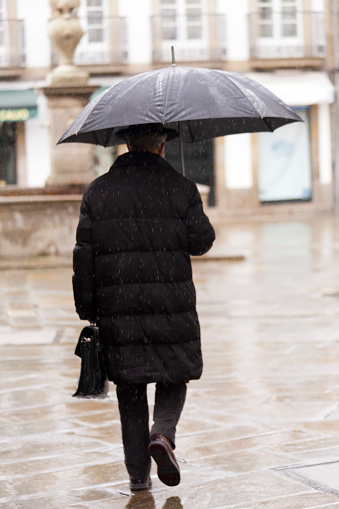 Cropped shot of a handsome young businessman holding an umbrella while standing in the rain outside during the day