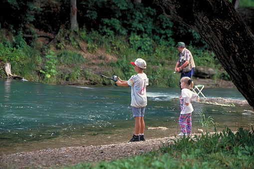 Roaring River State Park, Missouri USA June 13, 1998: A little girl watches her big brother fish while their grandfather casts in the background at Roaring River State Park in Missouri.