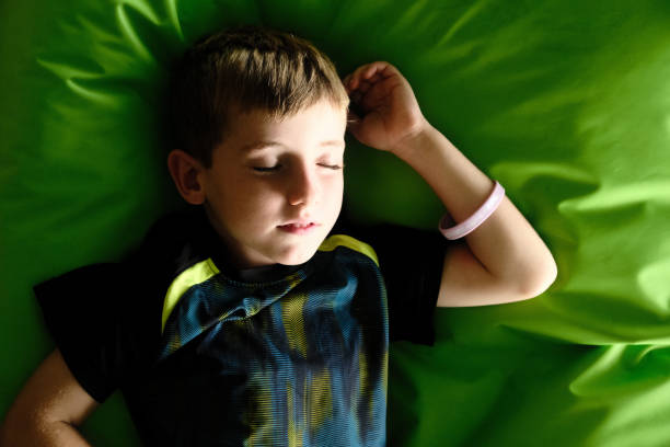 5-year-old boy sleeping on a large green pouf or cushion. He is dressed in sports clothes. He is resting during the day, with light coming in from the window. Calm and relaxed.