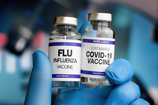 Flu and Covid-19 vaccine for booster for omicron and Influenza virus. Doctor Holding Coronavirus vaccine and Flu Shot vials for booster vaccination for new variants of Sars-cov-2 virus and Influenza