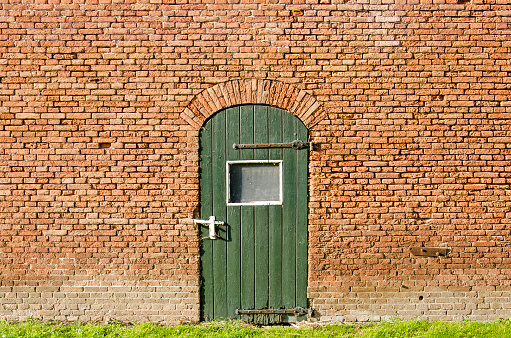 Old brick wall of a farm shed with a green wooden door