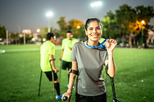 Portrait of a mid adult amputee female soccer player holding medal on soccer field