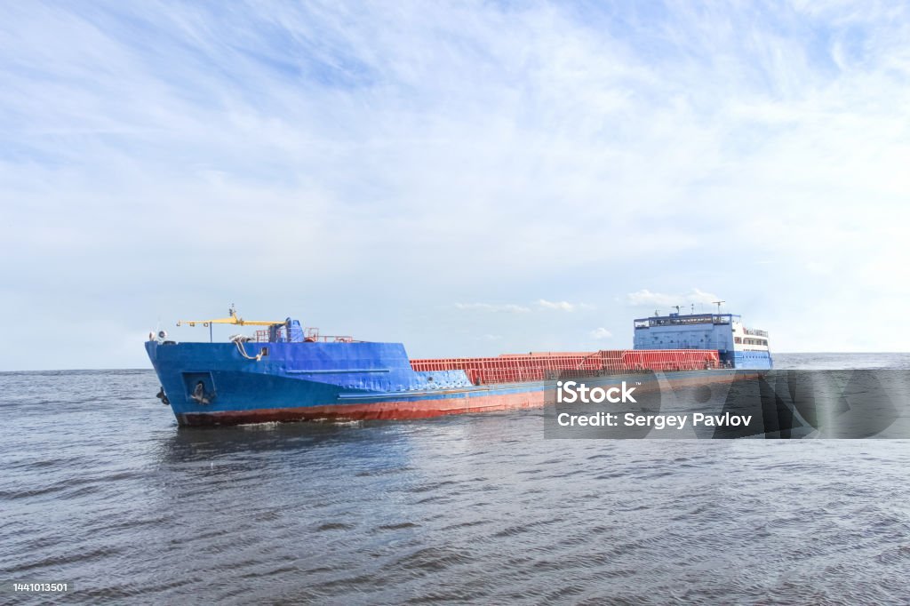 Cargo ship sailing on the boundless sea A cargo ship sailing on a calm boundless sea under a blue sky with sparse clouds Abstract Stock Photo