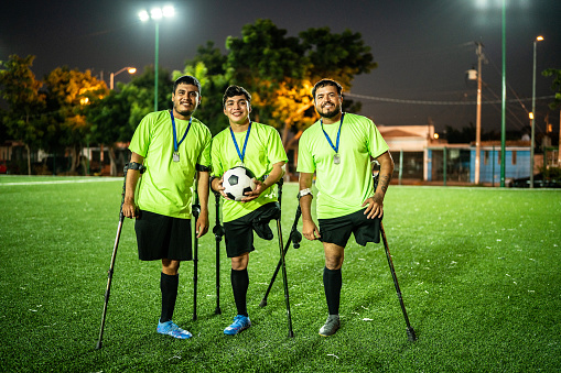 Portrait of amputee soccer players with medal while holding soccer ball on soccer field