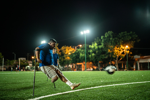 Mid adult amputee player hitting penalty kick on soccer field