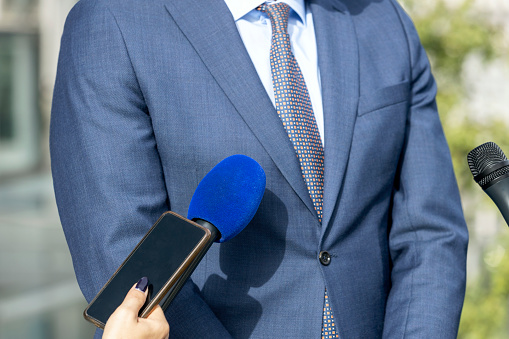 Reporter at news conference holding microphone and smartphone making media interview