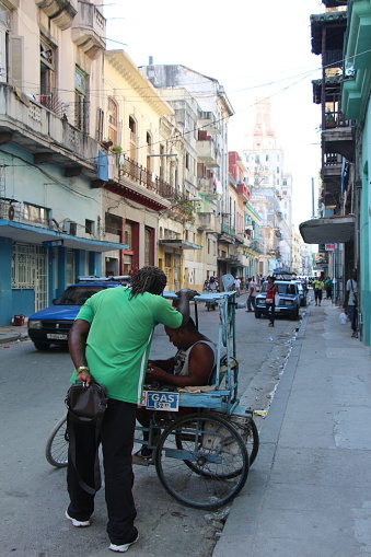 Cuba - two cubans talking on a street in the old town of havana. One of the two people is in a homemade three-wheeled vehicle - 08.09.2019