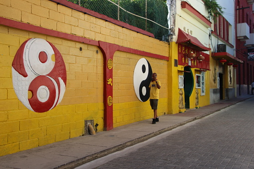 Cuba - La Havana -a man walking in havana's chinatown along a yellow wall where the ying and the yong are drawn - 08.09.2019