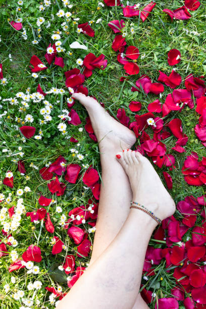 istock vertical image of unrecognizable barefoot woman's legs with red nails and anklet on grass and rose petals. with copy space. 1441025102
