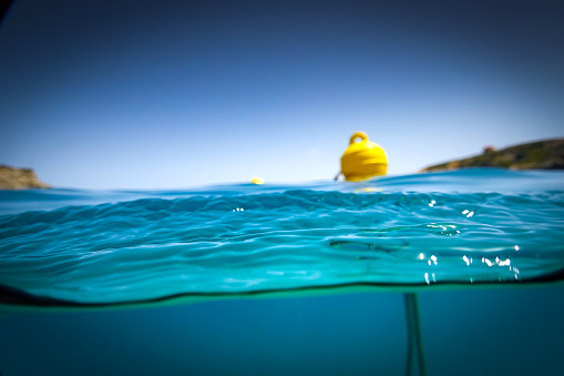 Yellow buoy floating on water surface of sea against clear blue sky during sunny day