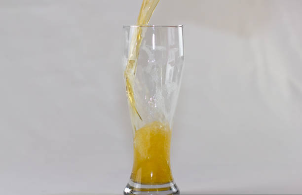 istock Light beer is poured into a glass on a white background. Beer flows down the walls forming a whirlpool, many bubbles and foam. Filling a beer glass. 1441025533
