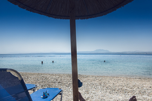 Deck chairs with thatched parasol at beach and scenic view of calm seascape against clear blue sky during sunny day