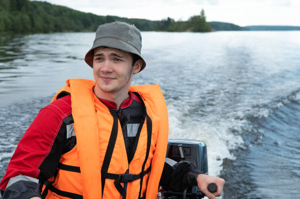 un jeune homme séduisant vêtu d’un gilet de sauvetage rouge conduit un bateau à moteur - motorboating sailing life jacket lake photos et images de collection