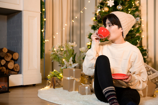 An Asian young woman wearing sweater enjoy winter season , reading book and drinking coffee at home