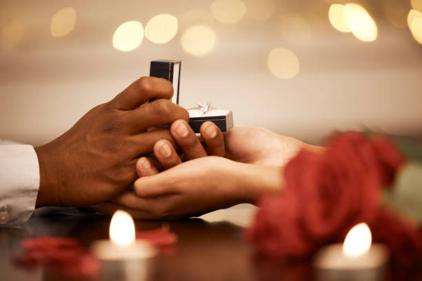 ring, love and marriage proposal with couple on a romantic date and holding hands while asking the big engagement question. commitment, anniversary and gift from a man to fiance woman to be engaged - men african descent giving flower imagens e fotografias de stock