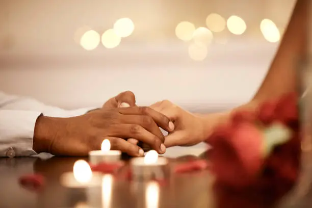 Photo of Couple holding hands at valentines table on date or romantic anniversary celebration together. Man touch black woman fingers, as expression of love at dinner with candles and rose petals