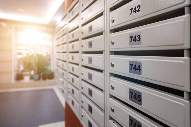 White Mailboxes in an apartment residential building at window with sun flare background. Backdrop of rows of numbered mailbox in residential apartment build. Correspondence concept. Copy text space