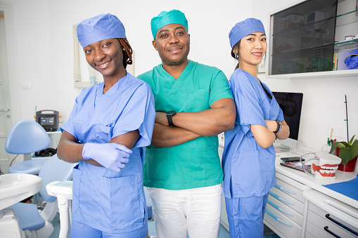 Three dentists pose smiling in a dental office, work in the health sector.