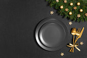 Festive empty table setting with golden Christmas decorations on a black background. View from above. Space for text.