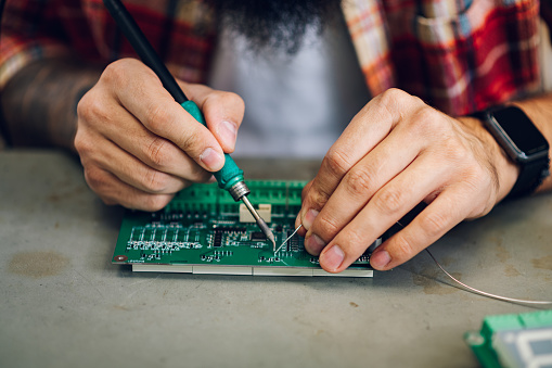 Close shot of electronics technician man hands soldering circuit board in his workshop. Computer support engineer. Modern technology. Repairing by hand. Fixing a mother board.
