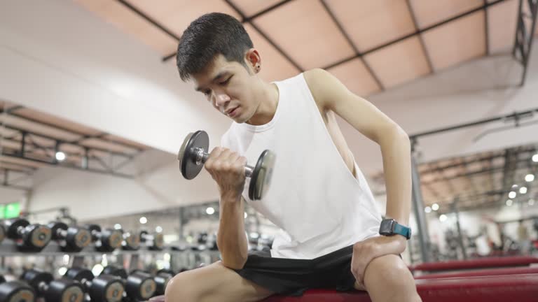 Skinny man doing seated one arm curl with a small dumbbell.