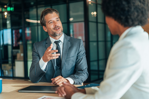 Couple of business persons talking in the office. African-american ethnicity business woman and mid aged businessman having meeting in modern office, discussing new ideas and building successful business together