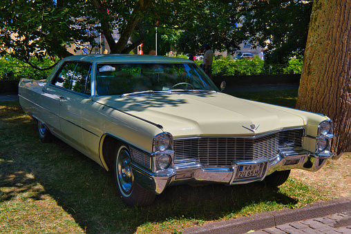 Baden-Baden, Germany - 10 July 2022:beige ivory white Cadillac de Ville Third 3rd generation 1965 sedan is parked in Kurpark in Baden-Baden at the exhibition of old cars \