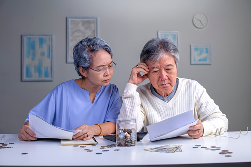 Worried Asian senior family couple reading financial documents or notification letter with bad news from bank while paying bills, retired husband and wife having money problems