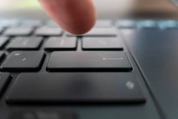 Photo of Finger pushing the button of keyboard. Click on black ultrabook key