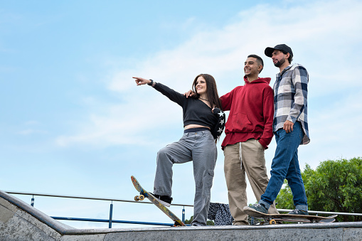 Group of Latin American skateboarder friends, chatting while laughing and enjoying together at a skatepark.