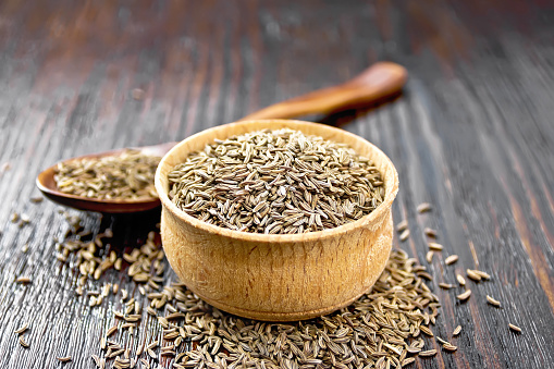 Cumin seeds in a bowl, spoon and on table against the background of wooden board