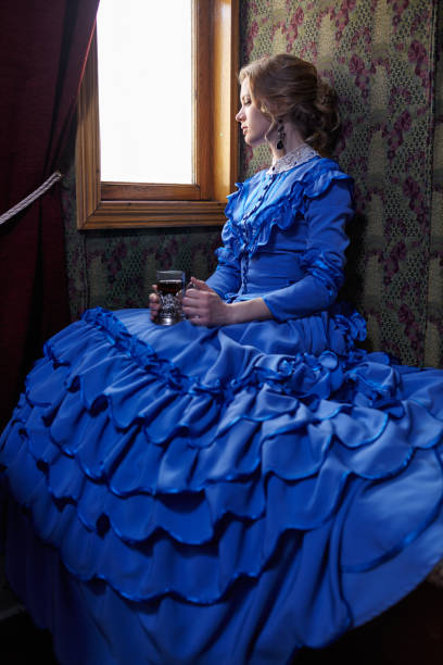 Young woman in blue vintage dress  sitting in coupe of retro railway train and drinking tea stock photo