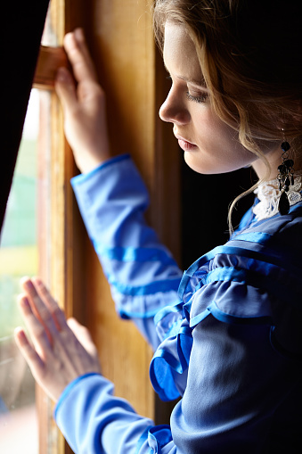 Young woman in blue vintage dress late 19th century standing near window in coupe of retro railway vehicle