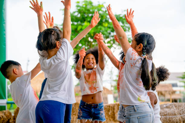 異なる民族の小さな子供のグループが手を上げたり歓声を上げたりして幸せを表現し、カラーペインティングで遊んだ後、服が多色で汚れます。 - child party group of people little girls ストックフォトと画像