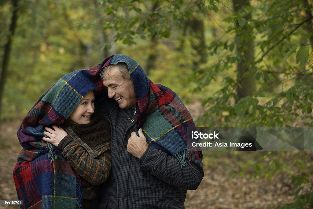 Sênior casal abraçando sob o cobertor na floresta - Foto de stock de 50-54 anos royalty-free